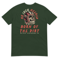 Vintage skull wearing a retro racing helmet with No Luck Needed Born of the Dirt graphic on a forest green T-shirt.